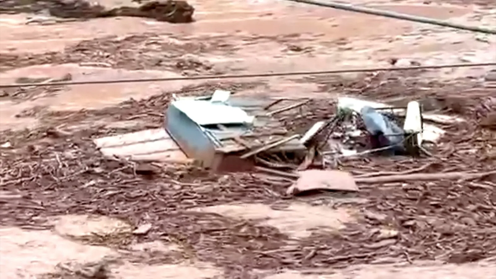 Muddy floodwater rushing through a Grand Canyon canyon floor with damaged footbridges